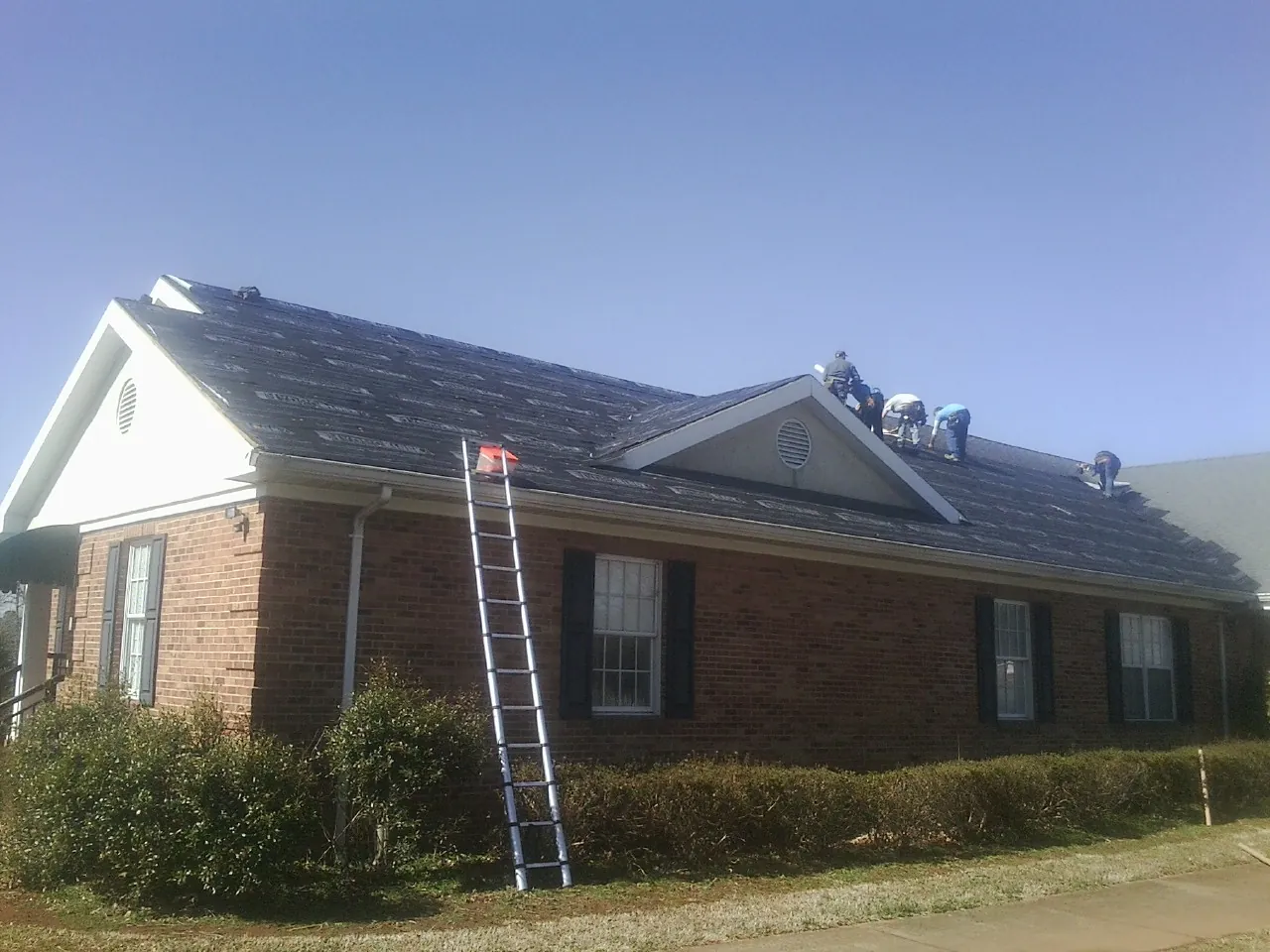 Crew tearing shingles off a brick ranch roof with a ladder set — Emergency Roof Repair work by our crew in Rockton