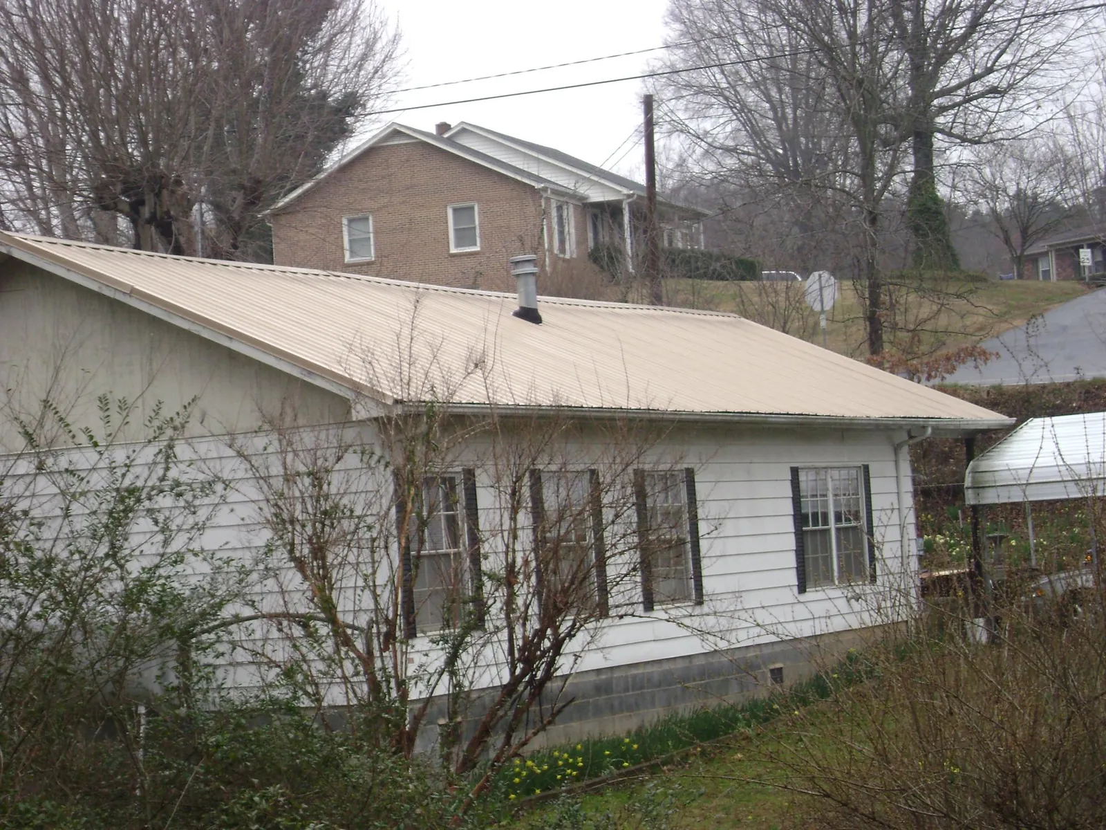 Tan metal roof on a white sided house set into a hillside — Commercial Roofing by Roofing Brothers in Rockton